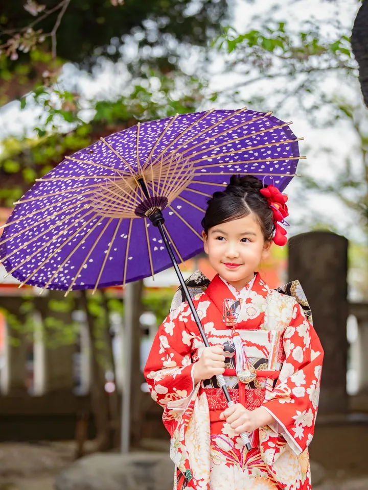 A 7-year-old girl in a Shichi-Go-San kimono, holding a purple Japanese umbrella.